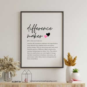 May include: Black and white printable wall art with the word "difference maker" in a cursive font. The definition of the word is written below in a smaller font. Two pink and black hearts are above the word "maker".