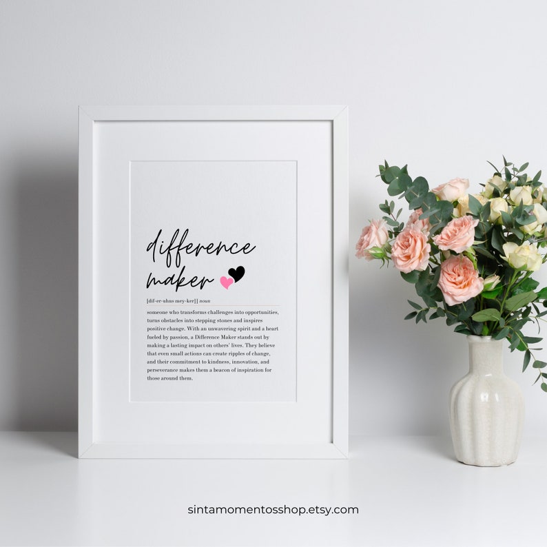 May include: A white framed print with a black and pink heart design. The print features the word "difference maker" with a definition below. The definition describes a difference maker as someone who transforms challenges into opportunities, turns obstacles into stepping stones, and inspires positive change. The print is on a white background and has a simple, modern design.