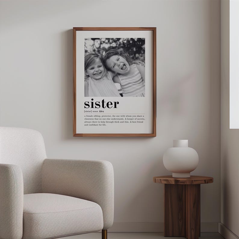 May include: Black and white photograph of two sisters smiling and laughing. The photo is framed and has the word "sister" with a definition below it.