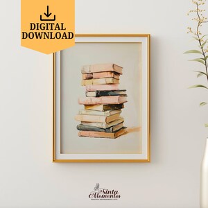 May include: A framed print of a stack of vintage books with pink and cream covers. The books are stacked in a tower and are slightly tilted to the right. The print is in a gold frame and is hanging on a white wall.