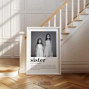 May include: Black and white photograph of two sisters standing side by side. The photo is framed in a white frame and has a definition of the word "sister" below the photo. The definition reads: "[sister] noun Hannah. A female sibling, protector, the one with whom you share a closeness that no one else understands. A keeper of secrets. Always there to help through thick and thin. A best friend and confidant for life."