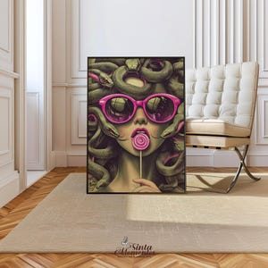 May include: A framed art print featuring a stylized illustration of Medusa wearing pink sunglasses and holding a lollipop. Her hair is composed of green snakes. The artwork has a modern, pop art style with vibrant colors and bold lines.