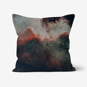 May include: Square throw pillow featuring a nebula design in shades of dark blue, red, and white. The pillow has a celestial theme with a starry night sky pattern, suitable for home decor.