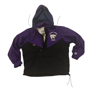Puede incluir: Una chaqueta cortavientos de color morado y negro con capucha. La chaqueta tiene un logotipo de los Kansas State Wildcats en la parte delantera con el texto "Kansas State" y "Bowling".
