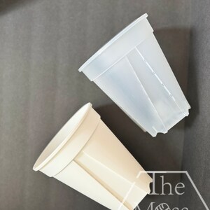 May include: Two plastic plant pots, one white and one clear, with a hexagonal design. The pots are on a gray surface with the text "The Moss Pole" printed on it.