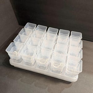 May include: A clear plastic seed starting tray with 24 individual square pots. The tray is white and sits on a dark surface. Each pot has a small drainage hole.