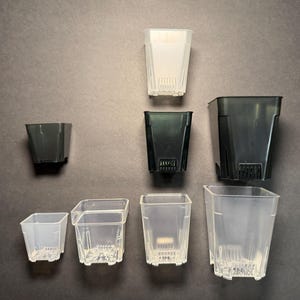 May include: An assortment of square plastic plant pots in various sizes and colors. The pots range from small, clear containers to larger, dark green and black pots. All pots have drainage holes at the bottom, suitable for gardening and plant propagation.