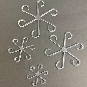 May include: Four clear plastic snowflake-shaped ornaments. Each ornament has six curved arms extending from a central hub. The ornaments vary in size, with the largest at the top and the smallest at the bottom.