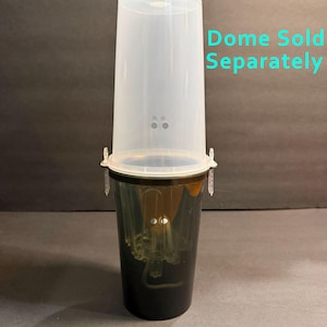 May include: A dark-colored plastic cup with a clear, translucent plastic dome lid attached to the top. The dome features small ventilation holes and two clear plastic clips on the sides. The text "Dome Sold Separately" is printed in light blue.