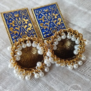 Pode incluir: Um par de brincos de ouro com desenhos florais azuis e dourados e detalhes de p&eacute;rolas brancas.