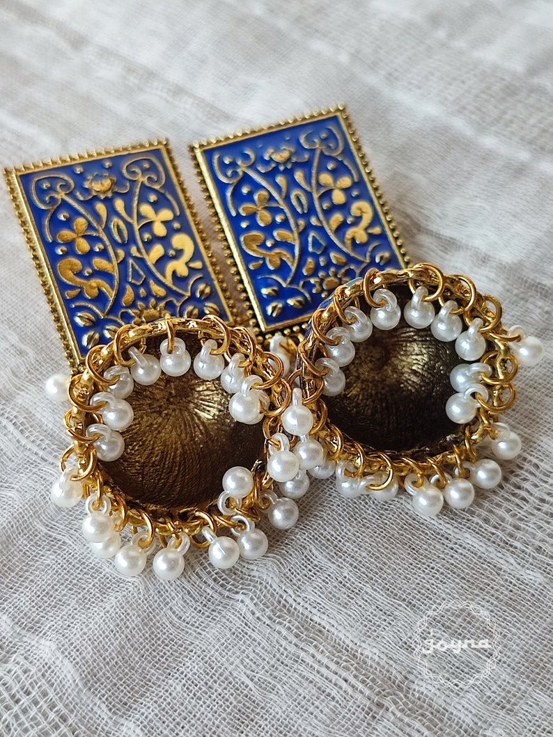 Pode incluir: Um par de brincos de ouro com desenhos florais azuis e dourados e detalhes de p&eacute;rolas brancas.