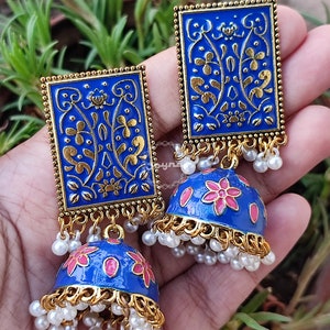 Pode incluir: Um par de brincos azuis e dourados com um design floral. Os brincos s&atilde;o feitos de metal e t&ecirc;m uma forma de sino pendente com p&eacute;rolas brancas.