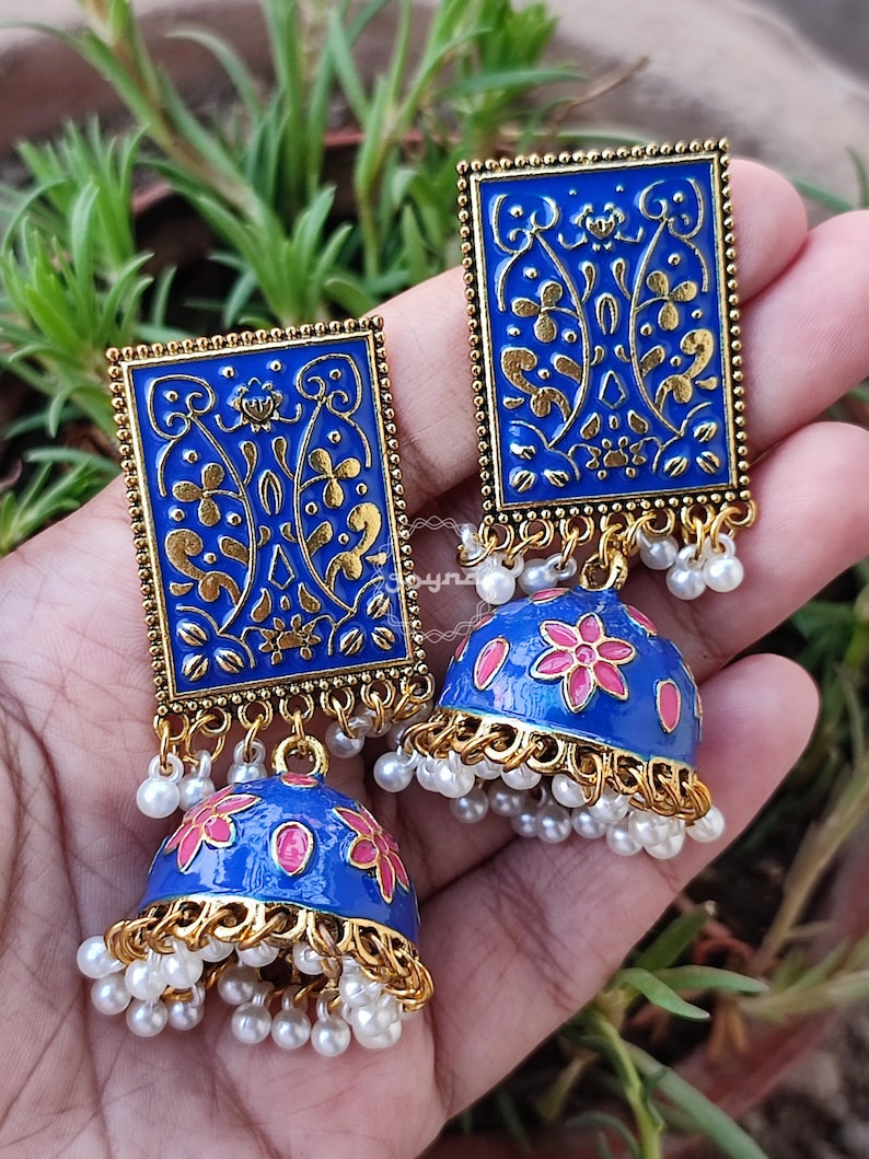 Pode incluir: Um par de brincos azuis e dourados com um design floral. Os brincos s&atilde;o feitos de metal e t&ecirc;m uma forma de sino pendente com p&eacute;rolas brancas.