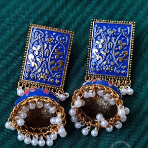 Pode incluir: Um par de brincos azuis e dourados com um design floral e detalhes de p&eacute;rolas brancas. Os brincos s&atilde;o de forma retangular e t&ecirc;m um pendente em forma de sino.