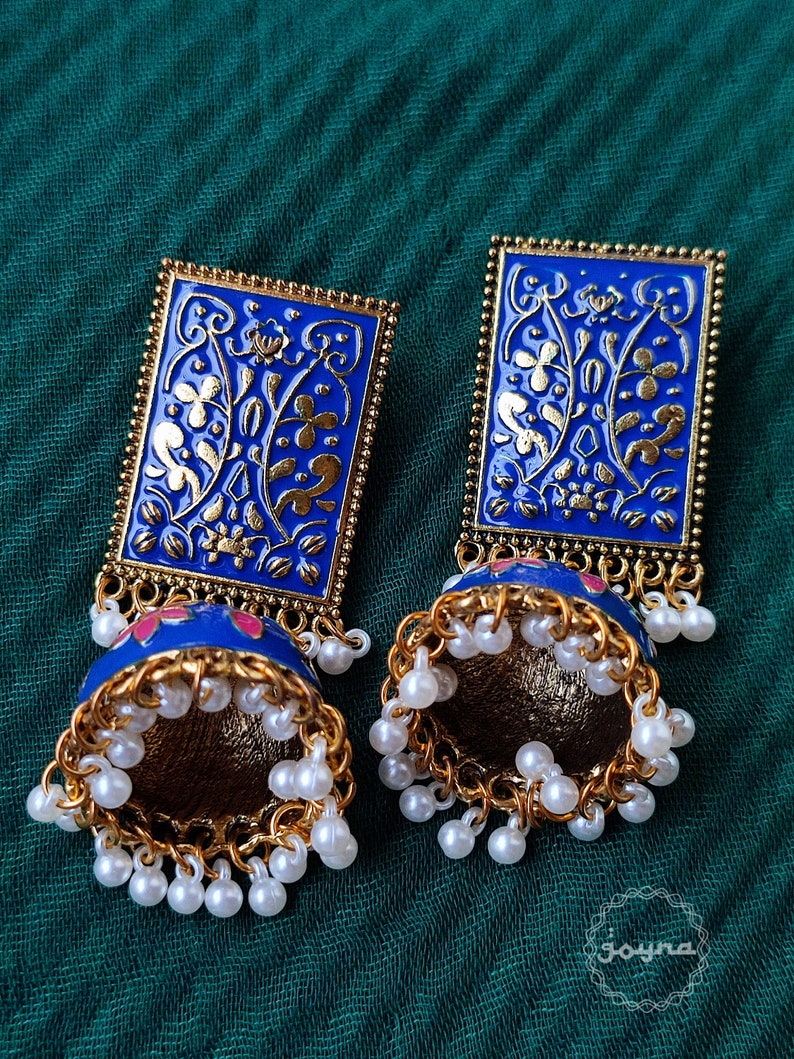 Pode incluir: Um par de brincos azuis e dourados com um design floral e detalhes de p&eacute;rolas brancas. Os brincos s&atilde;o de forma retangular e t&ecirc;m um pendente em forma de sino.