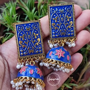 Pode incluir: Um par de brincos azuis e dourados com um design floral. Os brincos s&atilde;o feitos de metal e t&ecirc;m uma forma de sino pendente com flores cor-de-rosa. Os brincos s&atilde;o adornados com p&eacute;rolas brancas.