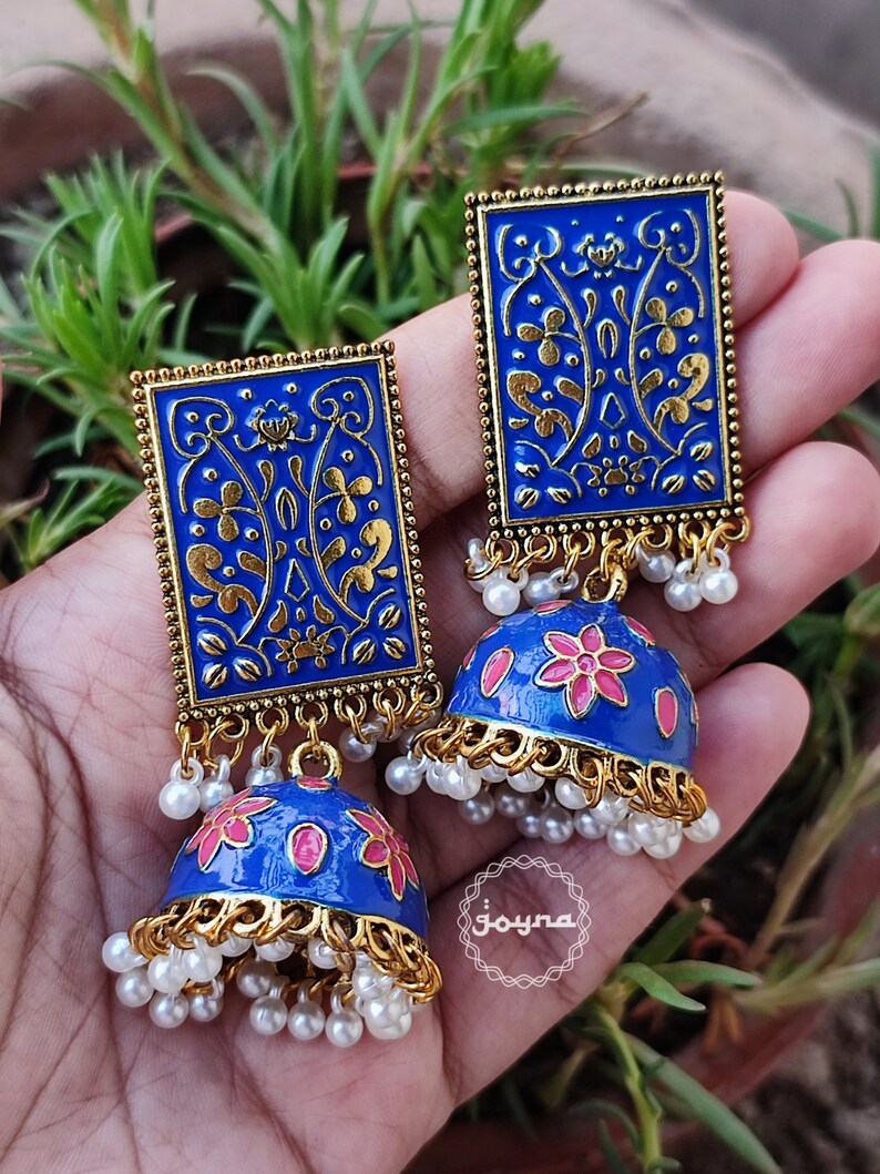 Pode incluir: Um par de brincos azuis e dourados com um design floral. Os brincos s&atilde;o feitos de metal e t&ecirc;m uma forma de sino pendente com flores cor-de-rosa. Os brincos s&atilde;o adornados com p&eacute;rolas brancas.
