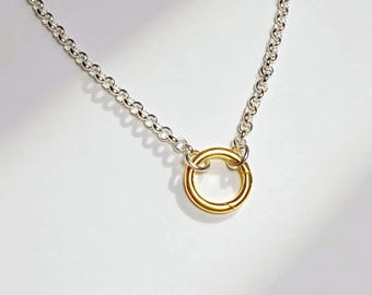 May include: A silver rolo chain necklace featuring a single circular gold-toned pendant. The chain consists of uniform round links connected to a smooth, polished gold ring that serves as the central focal point of the jewelry piece.