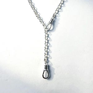 May include: A silver-coloured metal chain necklace featuring a Y-shaped design with a central connector link and a dangling clasp at the bottom. The chain is composed of round, interlocking links that create a continuous, polished metallic appearance.