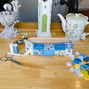 May include: A collection of decorative items including a bird-themed oil warmer, a bird sculpture, a teapot, a teacup, a pincushion, scissors, spools of thread, and buttons. The pincushion has blue floral fabric and the text "You are my sunshine".