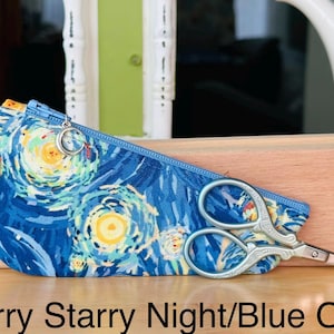 Op de afbeelding: Een blauw stoffen etui met rits, voorzien van een wervelend geel en blauw sterrenpatroon, een zilveren halve maan ritstrekker en een kleine zilveren schaar. De tekst Starry Starry Night/Blue Ombr&eacute; staat onderaan de afbeelding.