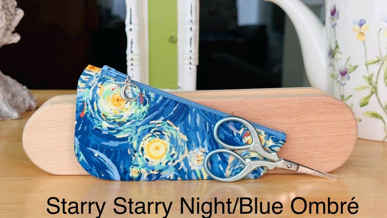 Op de afbeelding: Een blauw stoffen etui met rits, voorzien van een wervelend geel en blauw sterrenpatroon, een zilveren halve maan ritstrekker en een kleine zilveren schaar. De tekst Starry Starry Night/Blue Ombr&eacute; staat onderaan de afbeelding.