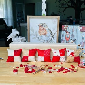 May include: A collection of decorative items on a wooden table. Includes small red and white patterned pillows, a framed bird print, a decorative sign that says "I'm in the Garden", and red-framed glasses.