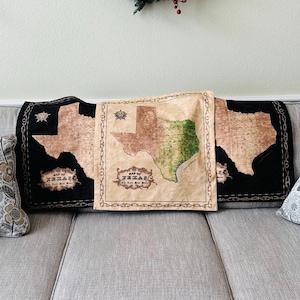 May include: A gray couch with two throw pillows featuring a floral pattern. A throw blanket with a map of Texas is draped over the couch.