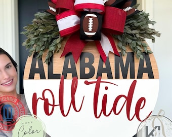 Op de afbeelding: Een rond houten deurbord met de tekst ALABAMA in het zwart en roll tide in rode schrijfletters. Het bord is afgewerkt met een grote decoratieve strik in rood, wit en zwart met football-afbeeldingen en groen kunstmatig gebladerte.