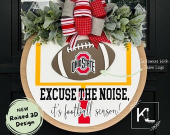 May include: A round wooden door hanger with a football, goal post, and the text "EXCUSE THE NOISE, it's football season!" The football has the Ohio State logo. The door hanger is decorated with a red and white striped bow and greenery.