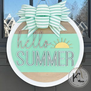 May include: A round wooden door hanger with a white border. The background is a light green with a brown wood grain stripe. The words "hello summer" are written in black with a white outline. A yellow sun with rays is to the right of the words. A green and white striped bow is at the top of the hanger.