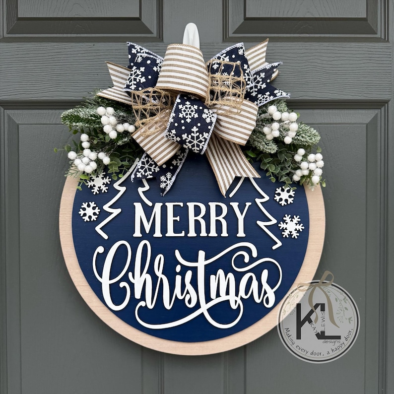 May include: A round wooden door sign with a dark blue center featuring the white text Merry Christmas and white snowflake accents. It is topped with a large bow made of navy blue snowflake ribbon and beige striped ribbon, plus white berry sprigs.