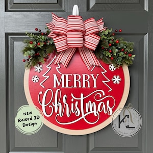 May include: A round wooden door sign with a red center featuring the white text Merry Christmas and two pine tree outlines. It is decorated with a red and white striped bow, green pine branches, red berries, and white snowflake cutouts.