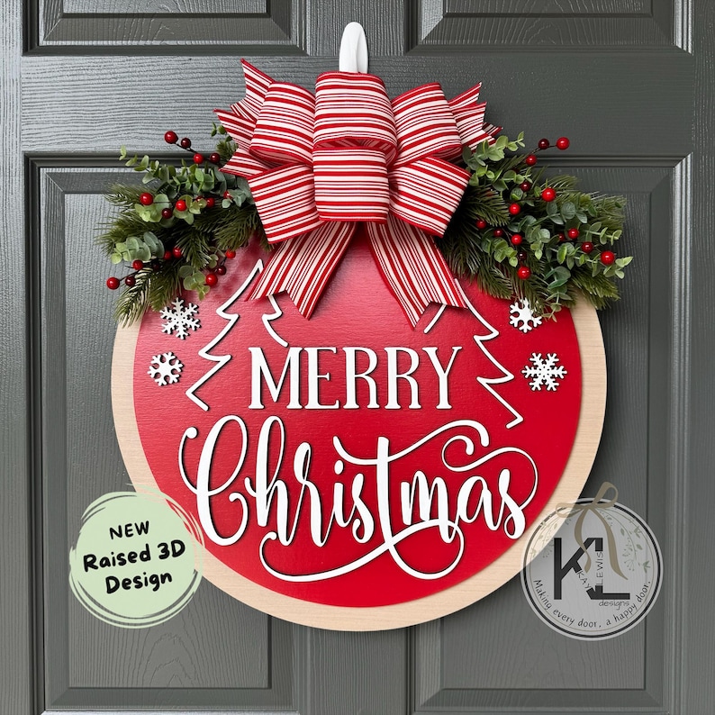 May include: A round wooden door sign with a red center featuring the white text Merry Christmas and two pine tree outlines. It is decorated with a red and white striped bow, green pine branches, red berries, and white snowflake cutouts.