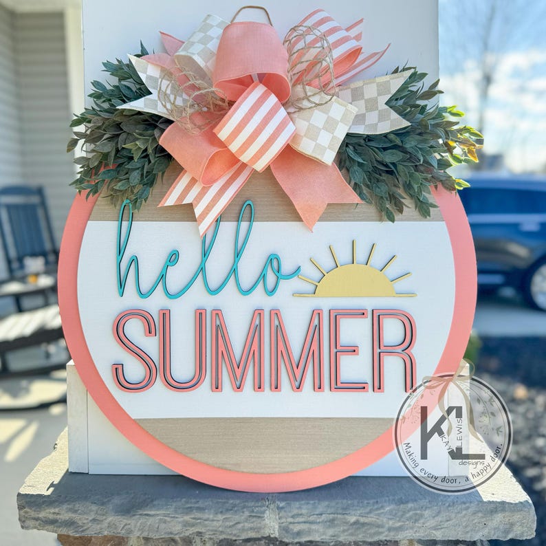 May include: A round wooden door hanger with a pink and white striped bow, green leaves, and the text "hello summer" in turquoise and pink lettering. A yellow sun graphic is above the text. The door hanger has a white and brown striped background.
