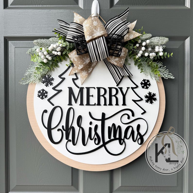 May include: A round wooden door sign with a white center and natural wood border. It features black cutout text reading Merry Christmas, black snowflake accents, and a large bow with beige and black striped ribbons and greenery.