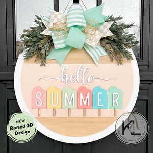 Pu&ograve; includere: Un appendiporta rotondo in legno con un bordo bianco. Il centro dell'appendiporta presenta uno sfondo in legno chiaro con il testo "hello summer" in bianco. Il testo "summer" &egrave; composto da cinque forme di ghiaccioli di diversi colori. L'appendiporta &egrave; decorato con un fiocco a scacchi verde e bianco e foglie verdi.