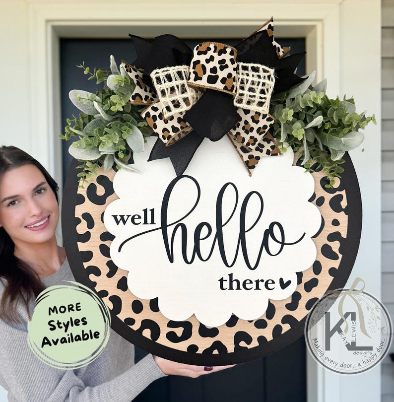 May include: Round wooden door sign with a black border and a leopard print design. The sign has the words "well hello there" in a cursive font. It is decorated with greenery and a bow with a leopard print pattern.