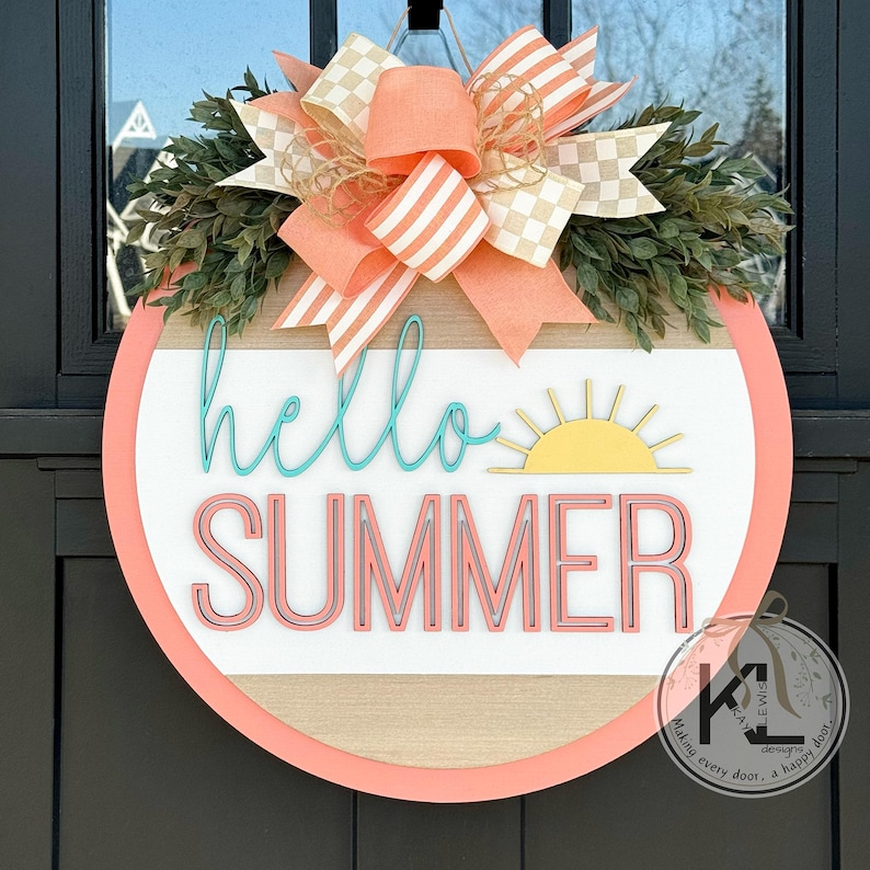 May include: A pink and white wreath with a wooden round sign that says "hello summer" in turquoise and pink lettering. The sign also has a yellow sun graphic.