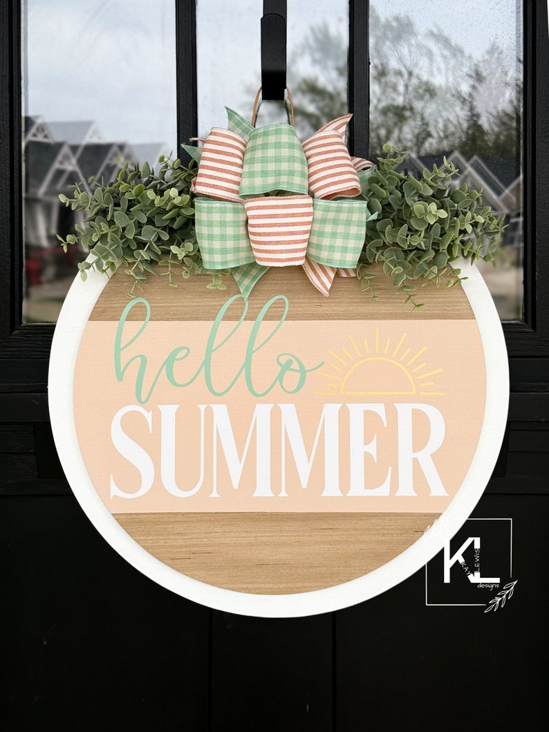 Pu&ograve; includere: Un appendiporta rotondo in legno con un bordo bianco. Lo sfondo &egrave; pesca con un sole giallo e il testo "hello summer" in verde e bianco. In alto c'&egrave; un fiocco di gingham verde e bianco con strisce pesca.