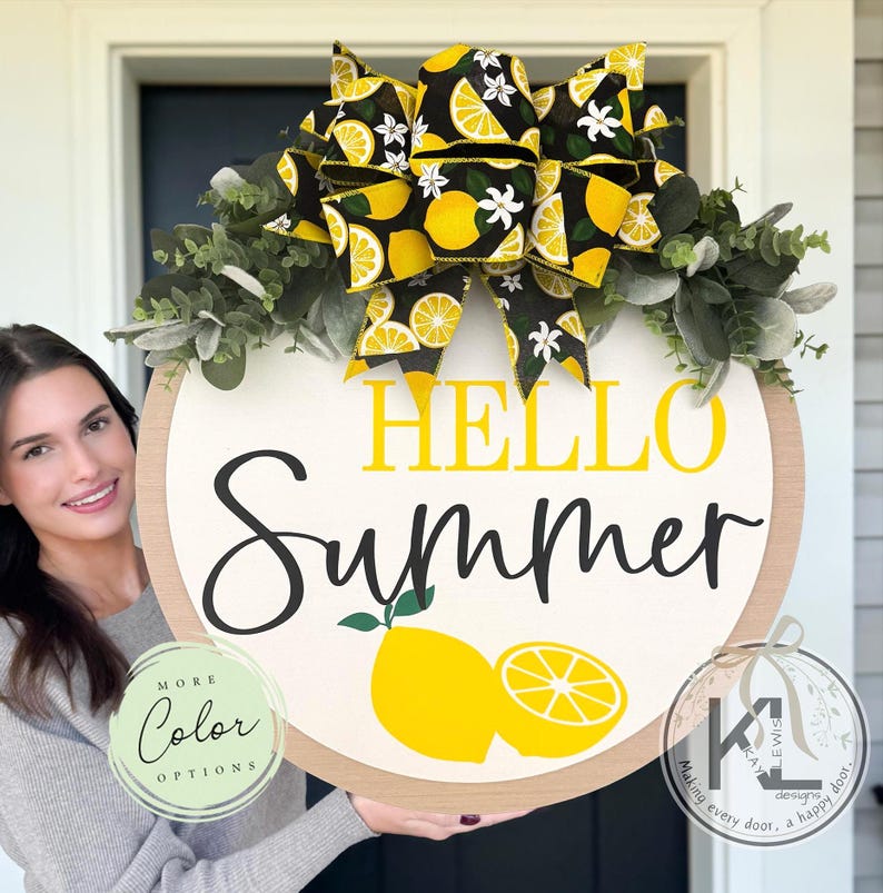Op de afbeelding: Een rond houten deurbord met de tekst HELLO SUMMER in gele en zwarte letters. Het bord is versierd met een grote strik met een patroon van gele citroenen en witte bloemen, geaccentueerd door groene eucalyptusbladeren en twee citroenafbeeldingen.