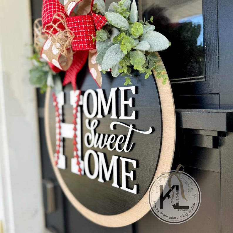 Peut inclure: Une pancarte en bois noir et blanc avec le texte "Home Sweet Home" sur le th&egrave;me du baseball. La pancarte est d&eacute;cor&eacute;e d'un n&oelig;ud rouge, blanc et marron et d'une guirlande de feuilles vertes.