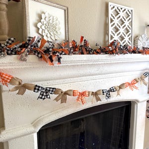 May include: A white fireplace mantel decorated with two garlands. One garland is made of burlap and fabric bows in orange, black, and white patterns. The other garland is made of fabric bows in orange, black, and white patterns.