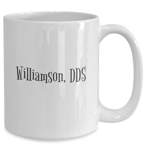May include: White ceramic mug with a curved handle. The mug features the text "Williamson, DDS" in a black, handwritten-style font. The mug is a standard size and shape, suitable for hot or cold drinks.