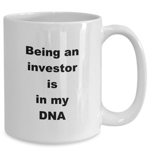 Op de afbeelding: Witte keramische mok met een gebogen handvat. De mok heeft de tekst "Being an investor is in my DNA" in zwarte, vette letters. Ontworpen voor warme dranken.