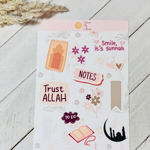 May include: A sticker sheet featuring Islamic-themed designs. The stickers include the phrases "Trust ALLAH" and "Smile, it's sunnah", alongside illustrations of a prayer rug, flowers, a mosque, and an open book. The website address "www.hennabyaleena.com" is also visible.