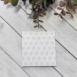 May include: A white card with a pattern of small, gold-colored flowers.
