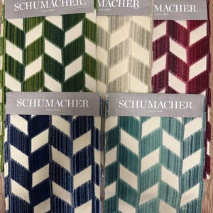 Puede incluir: Muestras de tela en tonos de verde, gris, burdeos, azul y turquesa con un patrón de chevrón. Cada muestra tiene una etiqueta que dice "SCHUMACHER since 1889". La tela tiene una apariencia texturizada.
