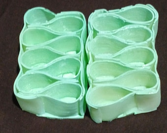 May include: Two sets of five light green, teardrop-shaped plastic organizers arranged in a vertical column. Each individual unit features a smooth, curved wall structure with an open top, designed to hold small items in a compact, modular configuration.