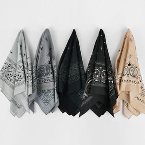 May include: Five bandanas in various colors hang against a white wall. The bandanas include light gray, dark gray, black, and tan. Each bandana features a paisley design in a contrasting color.